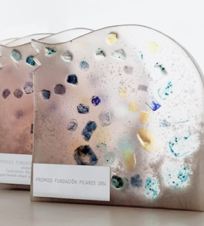 Premios con diseño artístico en tonos claros y detalles de colores, colocados sobre una superficie. Cada premio tiene una placa con texto