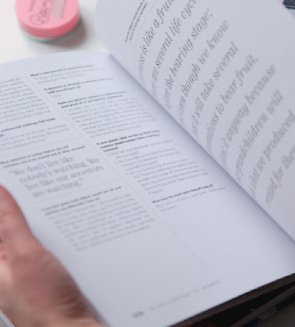Libro abierto con texto visible sobre una mesa, acompañado de un objeto redondo rosado en la esquina superior izquierda